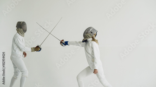 Young woman fencer having fencing training with trainer in white studio indoors