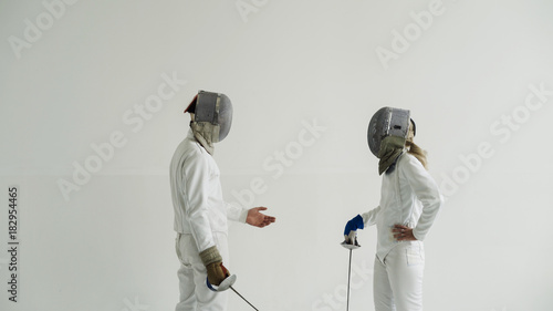 Two young smiling fencers man and woman sharing experience during break of fencing match indoors