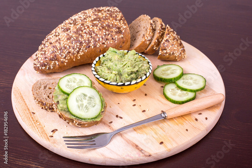 Traditional latinamerican mexican sauce guacamole in clay bowl, cucumber and avocado sandwiches on bread background.