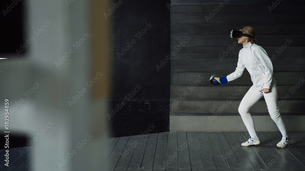 Concentrated fencer woman practice fencing exercises using VR headset and training simulator competition game indoors Concentrated fencer woman practice fencing exercises using VR headset and training simulator competition game indoors