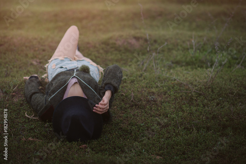 Fényképezés Portraif of woman lie supine on grass  and wearing black hat close her face