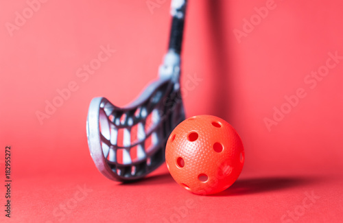 Floorball stick and ball against red background. Floor hockey concept.