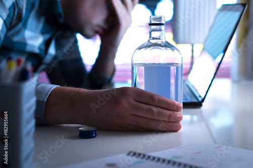 Alcoholism or drinking problem concept. Alcoholic with vodka bottle on table. Man and alcohol late at night. Drunk at work or in home office.
