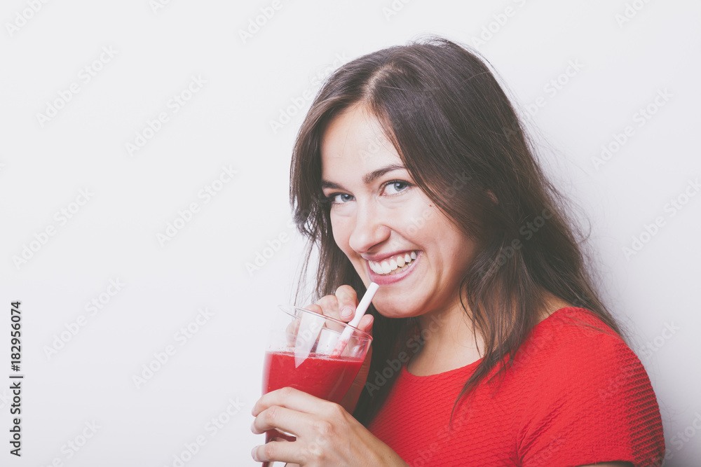 beautyful smiling brunette woman has a fresh red smoothie drink while she looks into your camera beautyful smiling brunette woman has a fresh red smoothie drink while she looks into your camera