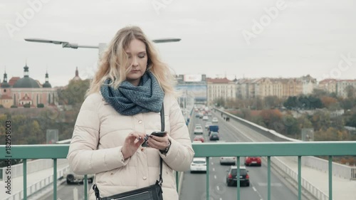 Attractive Tourist Dressed In Casual Wear Using Application On Smartphone For Navigating In Town, Hipster Girl Standing On Urban Setting Promotional Background Texting Messages via Mobile Phone photo