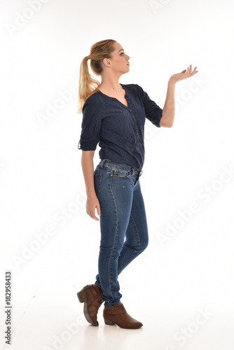 Full length portrait of a girl wearing simple blue shirt and jeans, standing pose side profile, on a white background.