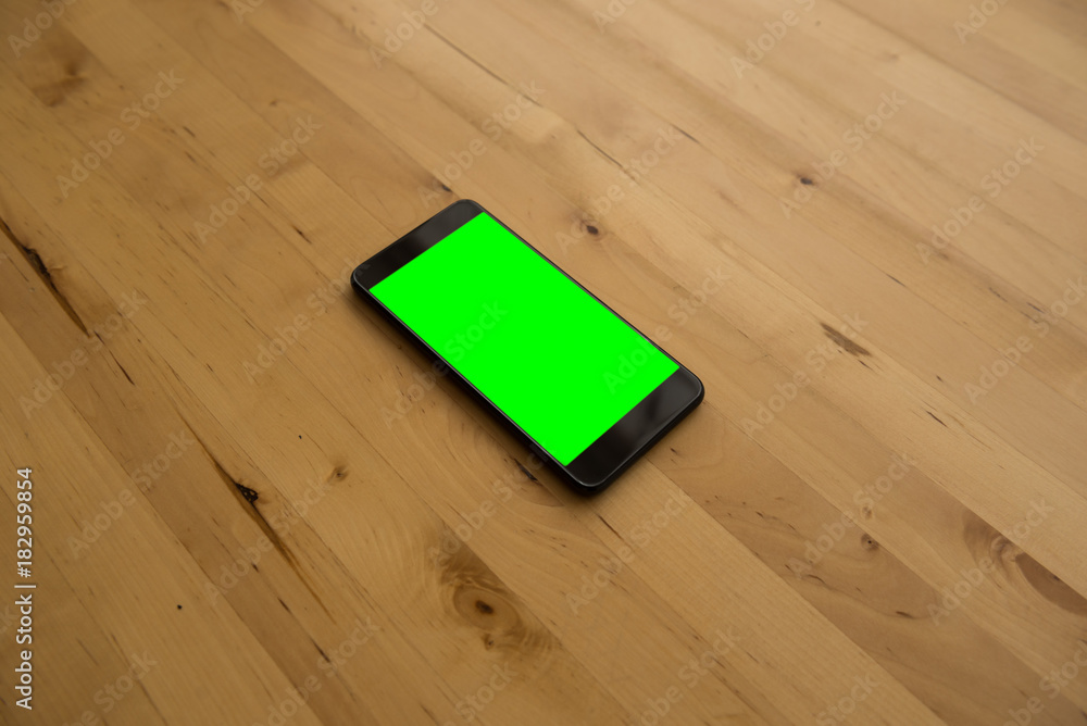 Green screen smartphone on wooden desk in bright office in the afternoon.
