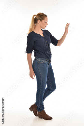 Full length portrait of a girl wearing simple blue shirt and jeans, standing pose side profile, on a white background.