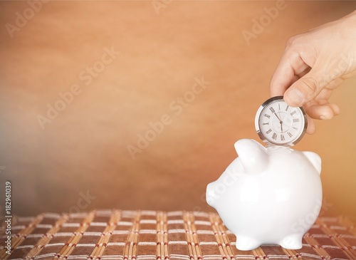 Hand holding watch and piggy bank on the table.