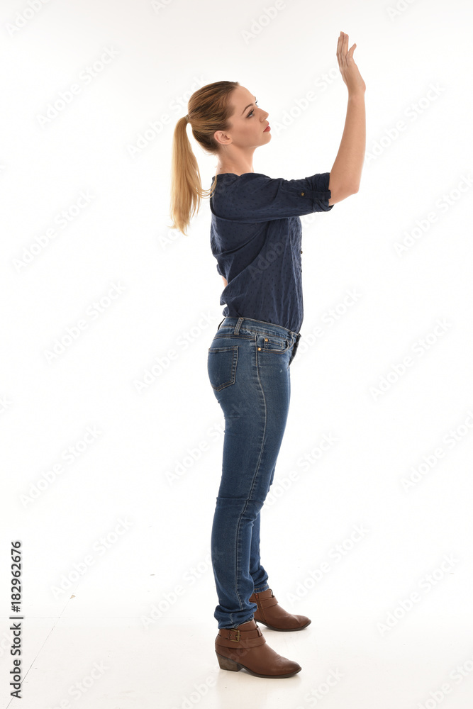 Full length portrait of a girl wearing simple blue shirt and jeans, standing pose side profile, on a white background. Full length portrait of a girl wearing simple blue shirt and jeans, standing pose side profile, on a white background.