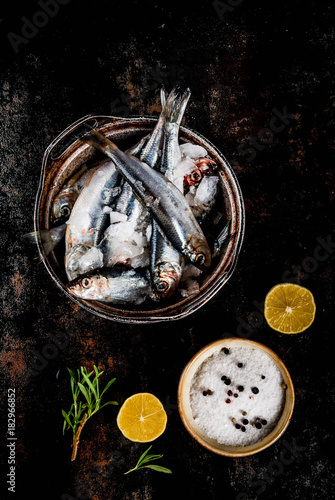 Fresh raw fish with rosemary, lemon and salt on dark rusty background, copy space top view