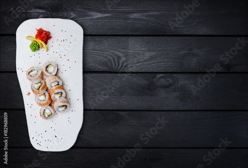Philadelphia roll with a cucumber, avocado, some cream cheese, tobiko caviar and shrimp. Top view. Black wooden background. photo
