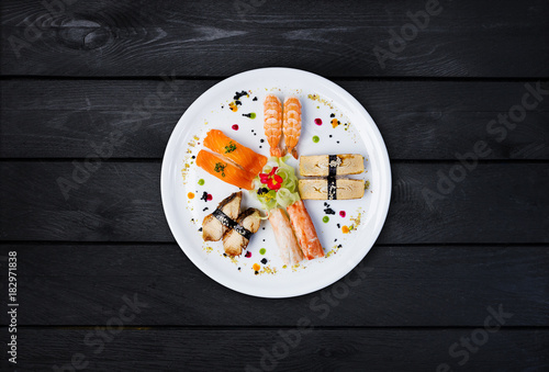 Sashimi set on a white round plate, decorated with small flowers, Japanese food, top view. Black wooden background