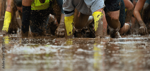 Mud race runners.Crawling,passing under a barbed wire obstacles during extreme obstacle race