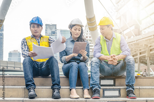 Three engineers sitting in front of building with blueprint on hand,Businessman,Engineers reading in blueprint instructions on hand in front of building