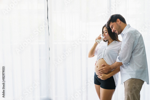 Beautiful pregnant woman standing and drinking milk with handsome husband at living room. concept of pregnancy  family  take care and lover relation.