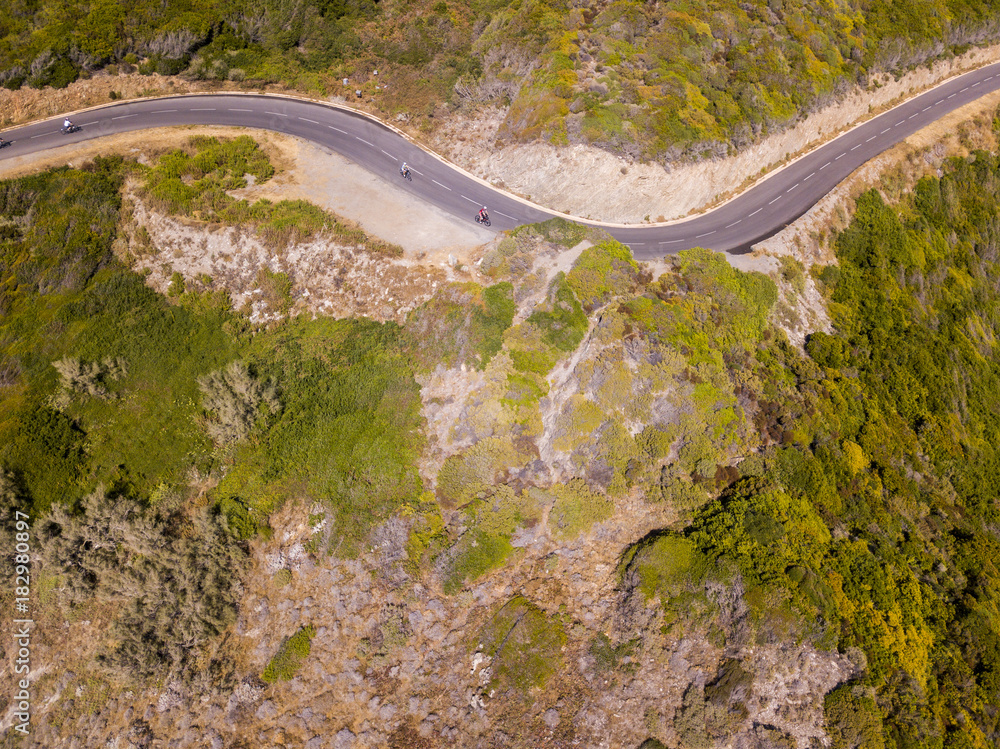 Vista aerea della costa della Corsica, strade serpeggiant. Ciclisti che corrono su una strada. Penisola di Cap Corse, Corsica. Tratto di costa. Anse d'Aliso. Francia