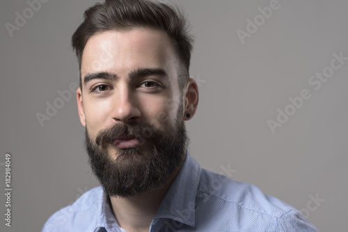 Close up horizontal portrait of stubble bearded smart casual business man with copyspace against gray studio background.