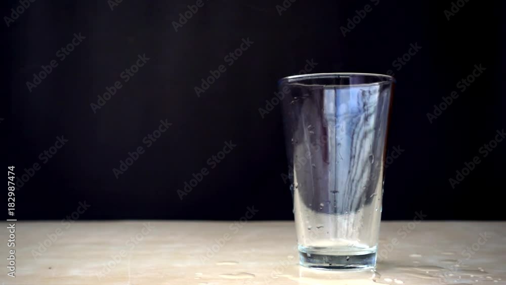 Pouring water into a glass on a wooden table on black background, Slow motion Pouring water into a glass on a wooden table on black background, Slow motion
