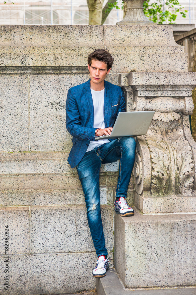 European college student studying in New York. Wearing blue blazer, jeans,  sneakers, a young guy staying at quiet corner on campus, working on laptop  computer, reading, thinking. Working Anywhere.. Photos | Adobe