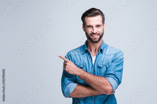 Have you seen this? Handsome young man pointing away and looking at camera with smile while standing against white background