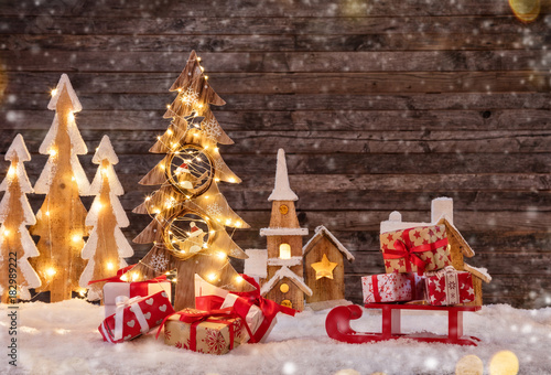 Holidays background with illuminated Christmas tree, sledge with gifts and wooden village.