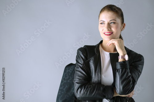 Portrait of beautiful young brunette woman in stylish black jacket on gray photo