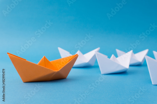 Business Leadership Concept - Yellow Color Paper ship Origami leading the rest of the white paper ship on blue background.