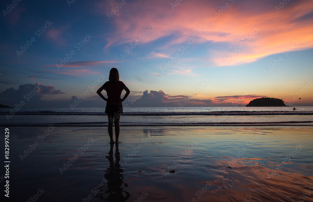 Silhouette of woman standing on the beach at sunset.