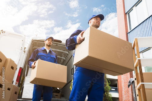 Close-up Of Two Delivery Men Carrying Cardboard Box photo