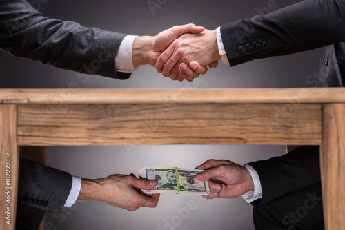 Businesspeople Shaking Hands And Taking Bribe Under Table photo
