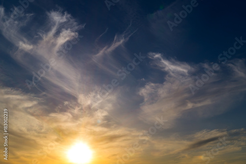 White striped curled clouds on the blue sky with sun on sunset or sunrise