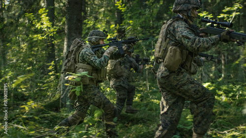 Squad of Fully Equipped Soldiers in Camouflage on a Reconnaissance Military Mission  Rifles in Firing Position. They re Running in Formation Through Dense Forest.