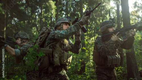 Fully Equipped Soldiers Wearing Camouflage Uniform Attacking Enemy, Rifles in Firing Position. Military Operation in Action, Squad Running in Formation Through Dense Forest. Side View Long Shot.