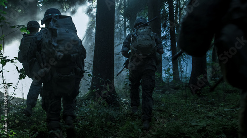 Fully Equipped Soldiers Wearing Camouflage Uniform Attacking Enemy, Rifles Ready to Shoot. Military Operation in Action, Squad Running in Formation Through Dark Dense Smokey Forest.