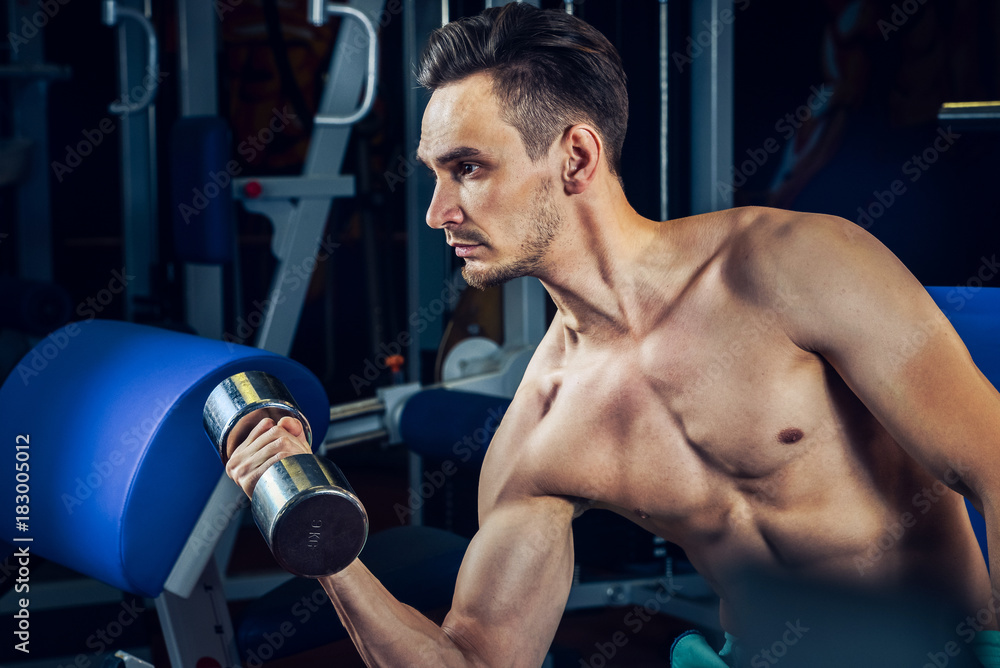 Handsome muscular man working out with dumbbells at gym. Bodybuilding, sport and fitness lifestyle. Handsome muscular man working out with dumbbells at gym. Bodybuilding, sport and fitness lifestyle.