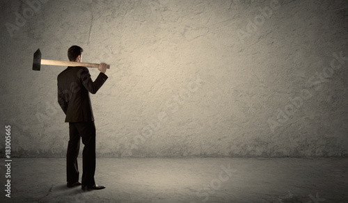 Business man standing in front of a grungy wall with a hammer