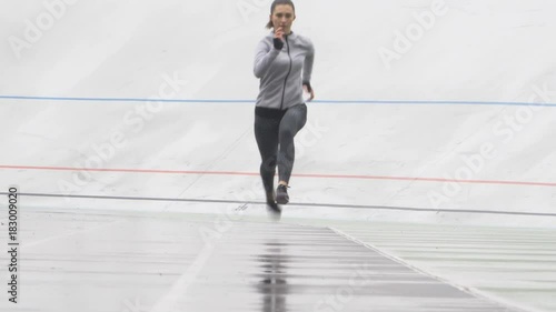 Female athlete sprinting in front of camera on a run path running athletic track