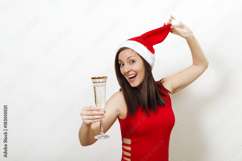 Beautiful caucasian young happy woman with charming smile in red dress and Christmas hat standing with glass of champagne on white background. Santa girl isolated. New Year 2018 holiday concept Beautiful caucasian young happy woman with charming smile in red dress and Christmas hat standing with glass of champagne on white background. Santa girl isolated. New Year 2018 holiday concept