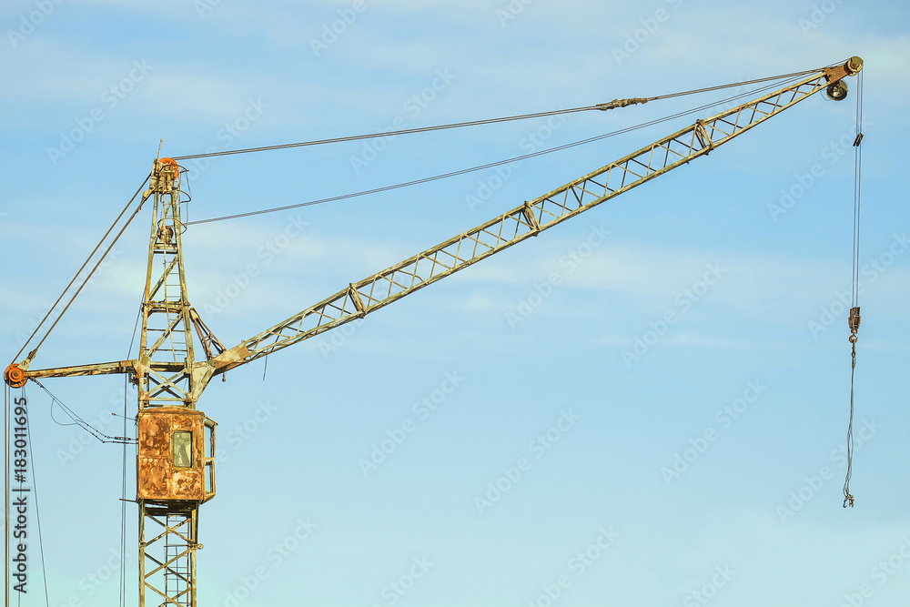 Old abandoned rusty tower crane on a blue sky background