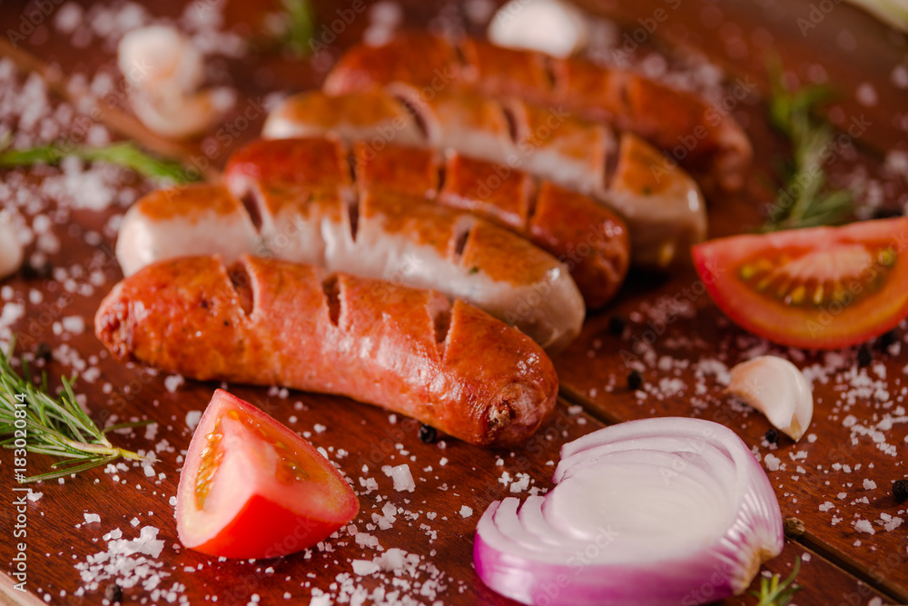 Close up of grilled sausages and vegetables, tomato and onion on a wooden background in rustic style Close up of grilled sausages and vegetables, tomato and onion on a wooden background in rustic style