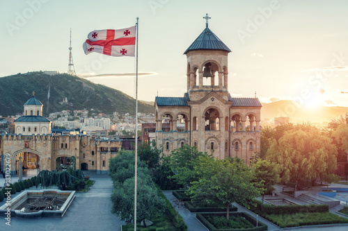 View of the sunset of the bell tower in Tbilisi, Georgia. And the flag of Georgia developing in the wind.