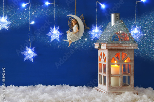 Wooden old house with candle and fairy on the moon over the snow and blue background.