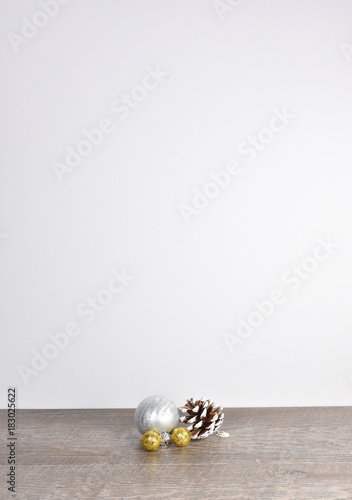 Simple Christmas scene including frosted pine cone and gold silver ornaments on weathered wood table with white background and copyspace