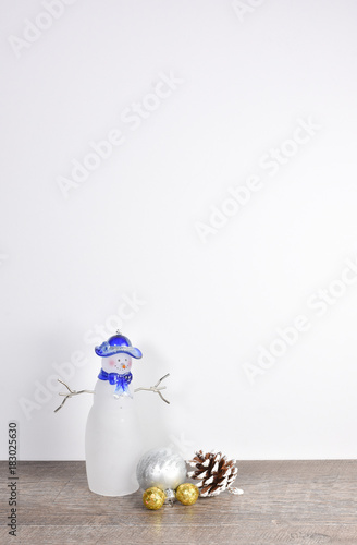 Simple Christmas scene including frosted pine cone, snowman, and gold silver ornaments on weathered wood table with white background and copyspace