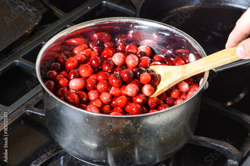 Cooking fresh red cranberries fto make cranberry sauce for Holiday dinner.  Wooden spoon stirs berries in stainless steel pot.