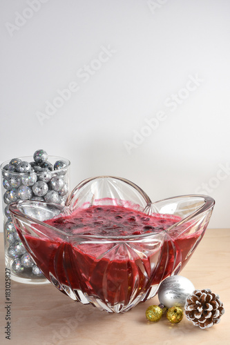 Homemade holiday cranberry sauces in crystal serving dish beside Christmas ornaments and frosted pine cone decorations.   White background copy space.