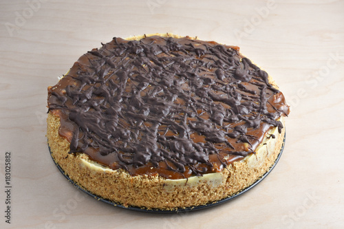 Beautiful turtle, chocolate and caramel covered, cheesecake with graham cracker and pecan nut crust on a wooden table.