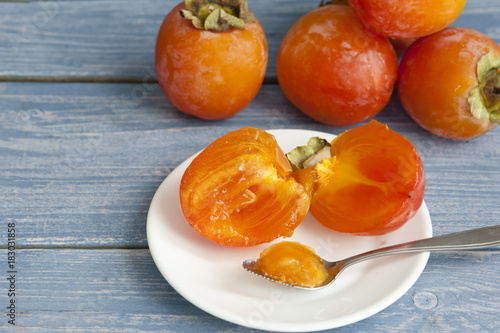 Fresh ripe persimmons in a bowl on a wooden table. Close-up.