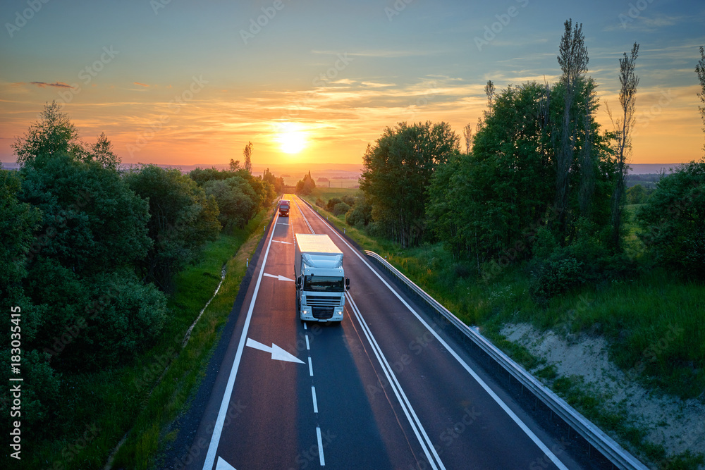 White truck and red one driving on the highway in a rural landscape at sunset. View from above.